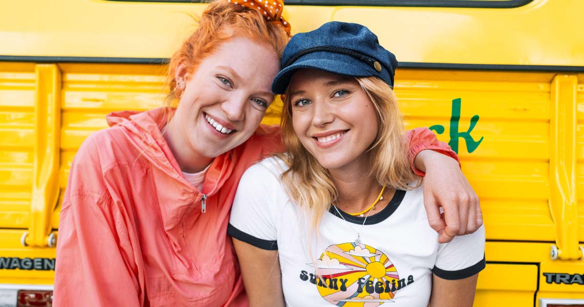 Två tjejer ler in i kameran mot gul bakgrund
